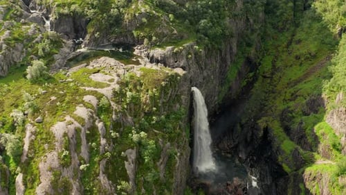 Drone Of Waterfall Cascading Over Cliff Into Lush Valley