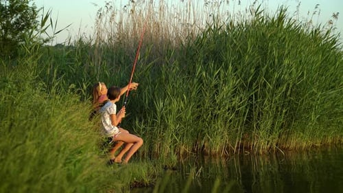 Kleine Mädchen mit Angelruten am Flussufer bei Sonnenuntergang