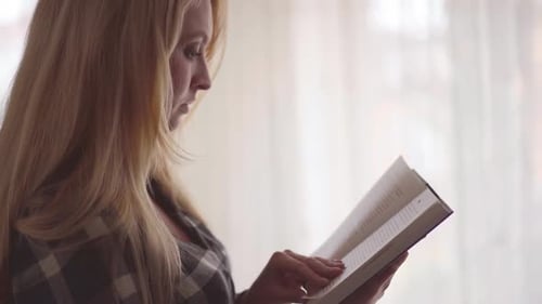 Portrait Cute Young Woman Reading Interesting Book in the Room in Front of Large Window Close Up