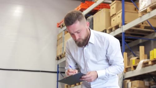 Man with a Beard Blue Shirt Inspects Warehouse with Boxes Goods Writes
