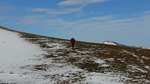 Aerial View of a Man with a Backpack Climbing a Snow Covered Mountain Against the Backdrop of a