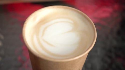 The girl picks up a cappuccino in a disposable glass. coffee house. close-up.