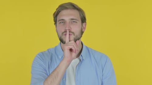 Young Man with Finger on Lips Silence Yellow Screen
