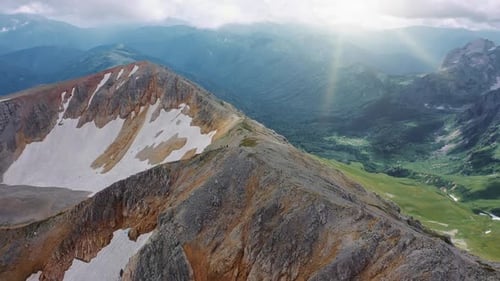 Luftaufnahme von einem braungrauen Berg mit Schnee bedeckt auf einem wunderschönen Tal der Berge, bedeckt