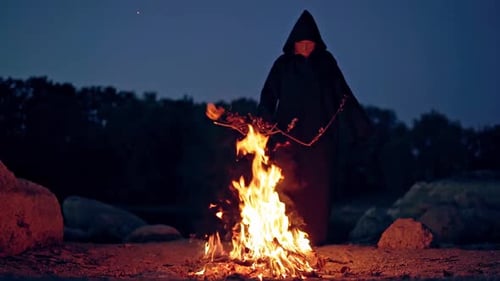 Figure in Robe Beside Campfire at Night