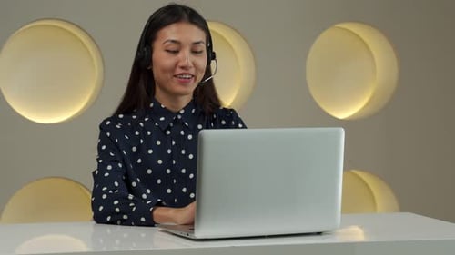 Smiling Asian Woman in a Headset Working in the Office As a Customer Support Service Sitting in the
