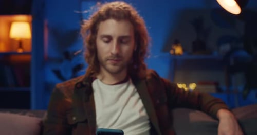Portrait of Long Haired Hipster Guy Looking at Smartphone Screen and Raising Head. Handsome Young
