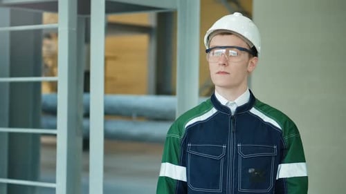 Young Engineer Wearing Protective Helmet Posing Looking at Camera at Modern Factory
