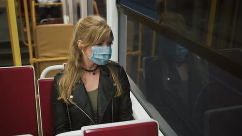 Woman Hipster in Medical Mask is Riding a Tram and Looking Out the Window
