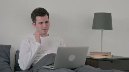Man Using Laptop in Bed Looks Tired