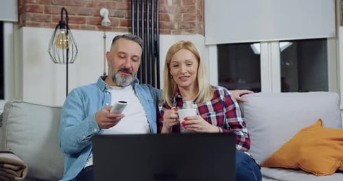 Casal relaxando no confortável sofá da casa e assistindo ao vídeo no laptop