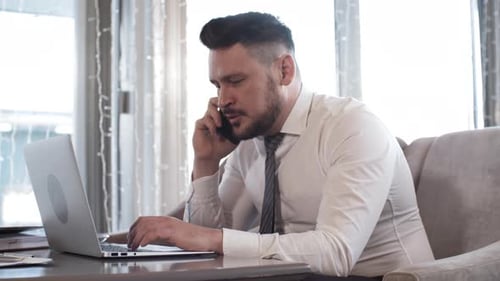 Man Talks on Phone While Working on Laptop
