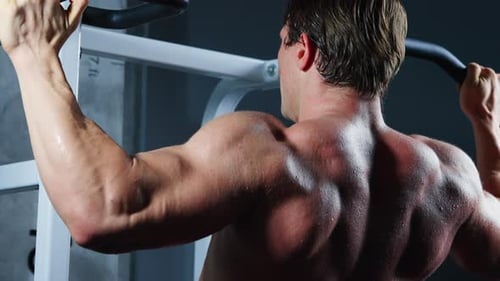 4K Caucasian man bodybuilder pulling up body weight lifting at gym.