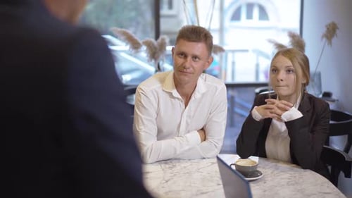 Young Caucasian Man and Woman in Formal Suits Sitting in Cafe and Talking with Unrecognizable