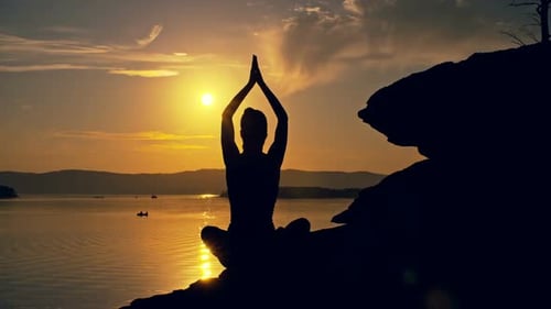 Silhouette Meditating on Rocky Lake at Golden Sunset