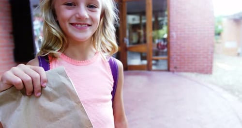 Portrait of happy schoolgirl holding paper bag in campus at school