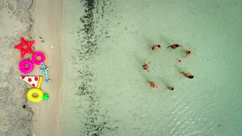 Aerial view of friends playing volleyball standing in sea by sandy beach.