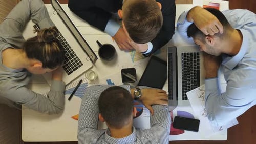 Vista superior de colegas cansados que se duermen sobre una mesa con computadoras portátiles y documentos en la oficina