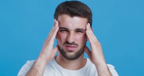 Young Man Suffering From High Blood Pressure, Massaging Temples and Grimacing, Close Up