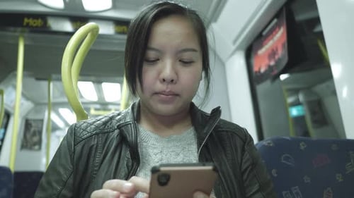 Front view of Asian woman sitting and using smartphone on a train