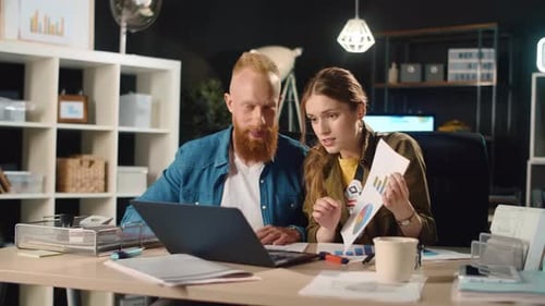 Young Business Couple Showing Documents in Front of Laptop Screen in Office