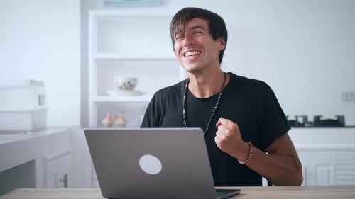 Man Celebrates Success Using Laptop at Home