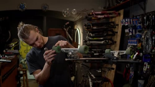 Young Man In The Workshop Attaches Wheel To Skateboard