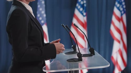 Professional Woman Speaks at Podium with Flags