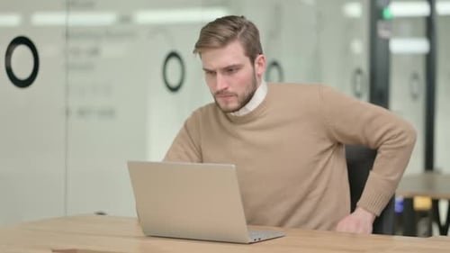 Creative Young Man with Laptop Having Back Pain in Office