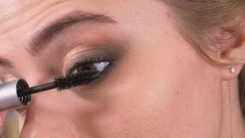 Makeup auftragen. Junges Mädchen schaut in den Spiegel und trägt Wimperntusche mit einem Pinsel auf die Wimpern von