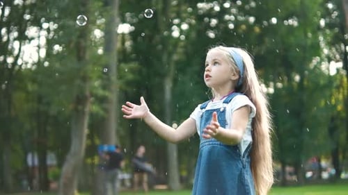 Little happy child girl chasing soap bubbles outdoors in summer park