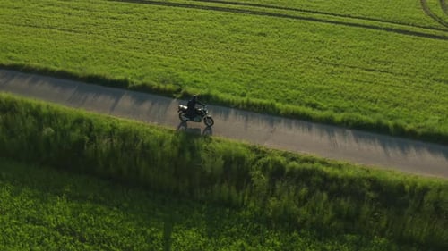 Motorcycle Driving on Rural Road Through Green Fields