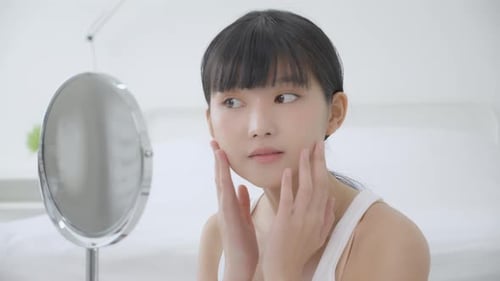 Woman Gently Touching Face in Front of Mirror