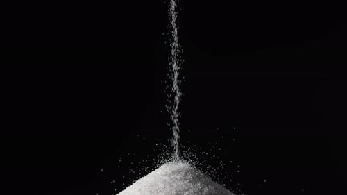Partikel aus weißem, trockenem Sand strömen hinunter und bilden einen Hügel auf einem isolierten schwarzen Hintergrund