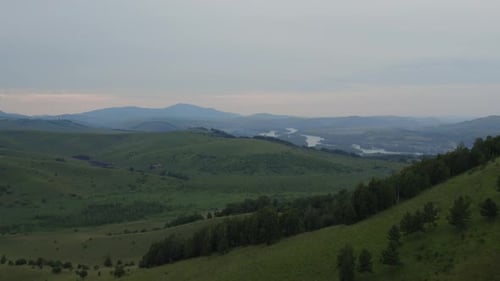 Green field and forest in valley under blue sky at during daytime