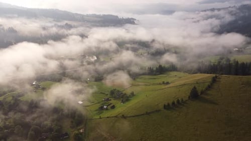 Flight Over a Small Village in the Mountains in the Summer Morning in the Fog