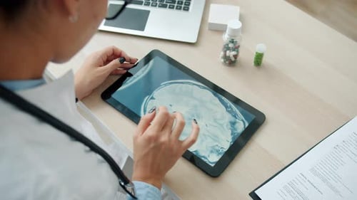 Junge Ärztin studiert MRT-Bilder auf Tablet-Bildschirm und arbeitet allein im Büro