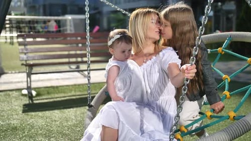 Mother and Daughters Together on a Swing in Park