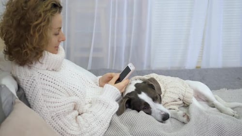 Woman Using Smartphone with Dog in Cozy Setting