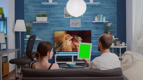 Young Woman Sitting Next to Boyfriend Holding Vertical Digital Tablet with Green Screen in Online