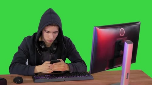 Hooded Hacker Using Laptop and Smartphone on a Green Screen, Chroma Key