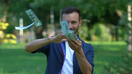 Aufgeregter bärtiger Mann wirft Dollar und lächelt im Park vor die Kamera, Lottogewinn