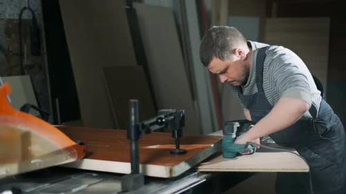 Man Smoothing Wood with Electric Sander in Workshop