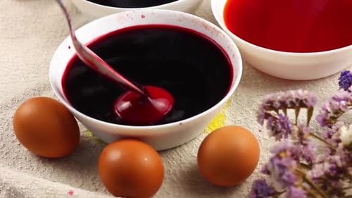Das kaukasische Kind bemalt ein Osterei mit einem Metalllöffel und taucht es in eine weiße Schale mit roter Farbe