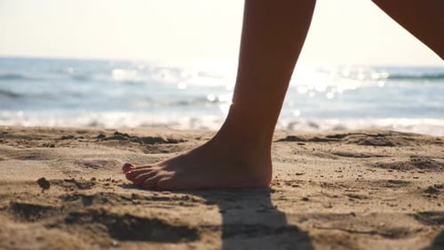 Close Up of Female Feet Walking on Golden Sand at the Beach with Ocean Waves at Background. Legs of