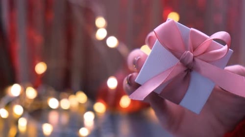 Hand Holding Gift Box with Pink Ribbon and Lights