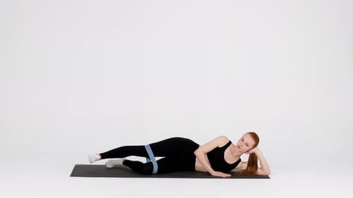 Woman Making Side Leg Lift Exercise With Elastic Rubber Band In Studio
