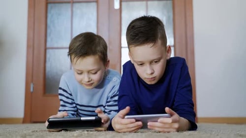 Two Boys Lying Down Using Technology Indoors