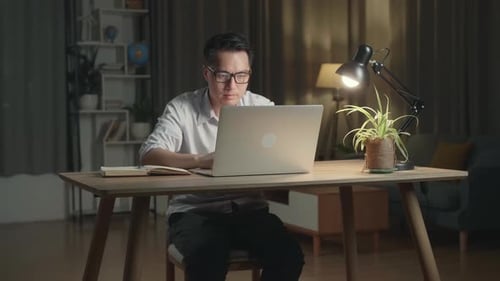 Asiatischer Mann, der zu Hause mit Laptop arbeitet, Überstunden in der Nacht