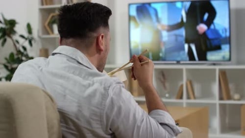 Man Eats Noodles While Watching Television at Home